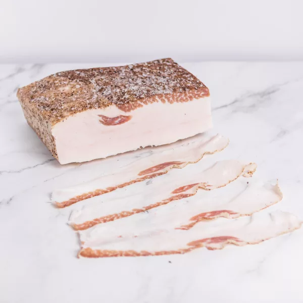 Lardo di Colonnata a fette sottili, presentato su un tagliere di legno con erbe fresche. My Little Italy