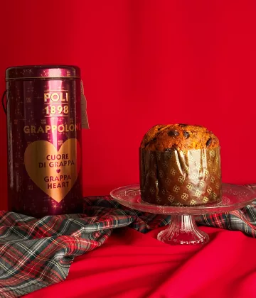 Panettone Grappa Poli Grappolone auf einer Kristallplatte mit violetter Sammlerschachtel mit goldenem Herz auf festlichem roten Hintergrund mit schottischem Stoff