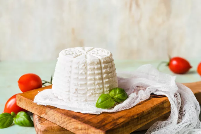 Photo de ricotta, un fromage historique italien, avec des feuilles de basiliques et des petites tomates.