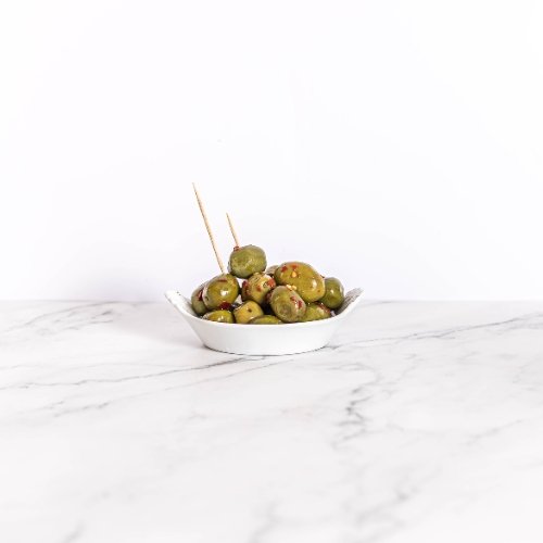 Bol de dégustation d'olives vertes piquantes épicées, présenté sur un fond de marbre élégant.
