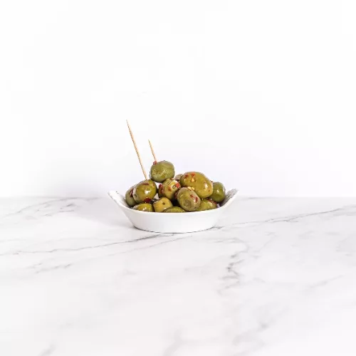 Bol de dégustation d'olives vertes piquantes épicées, présenté sur un fond de marbre élégant.