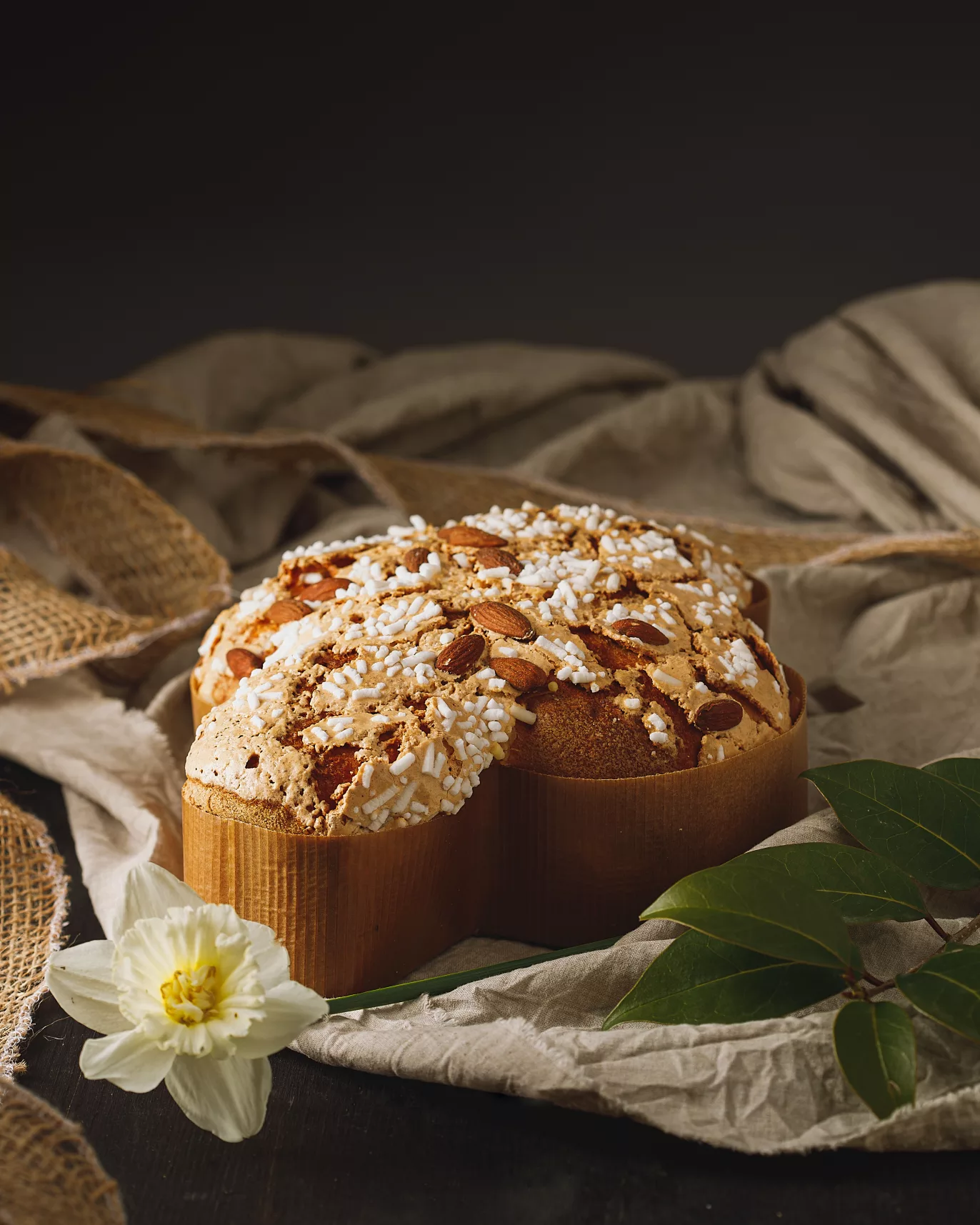Une colombe de paques présenté dans un décors avec un drap et une fleure, ambiance printanière.