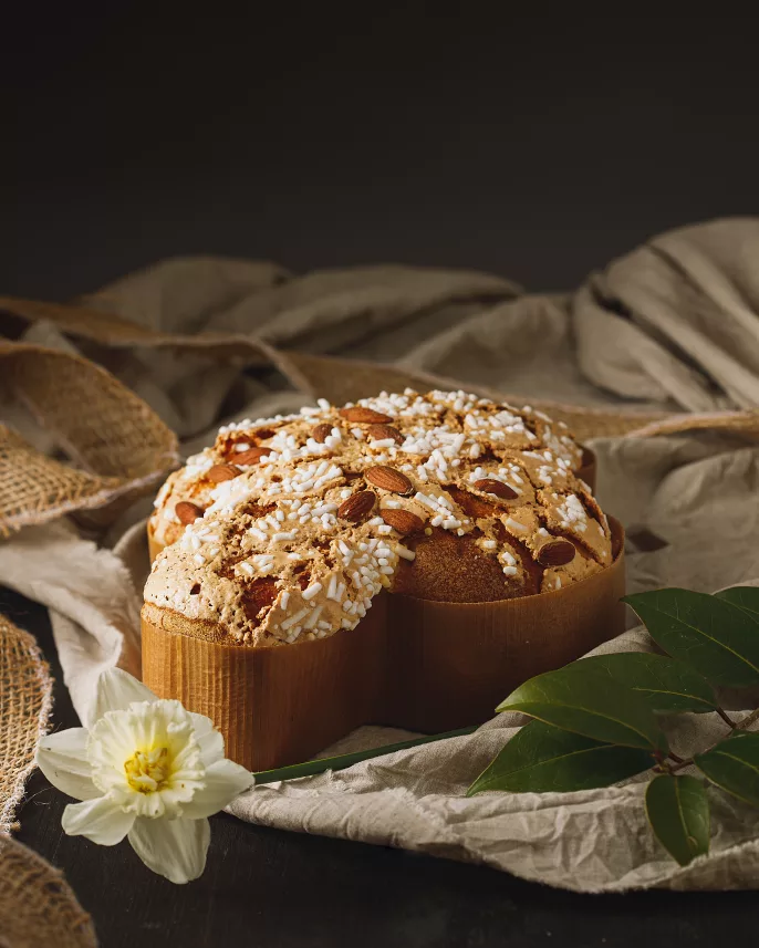 Une colombe de paques présenté dans un décors avec un drap et une fleure, ambiance printanière.