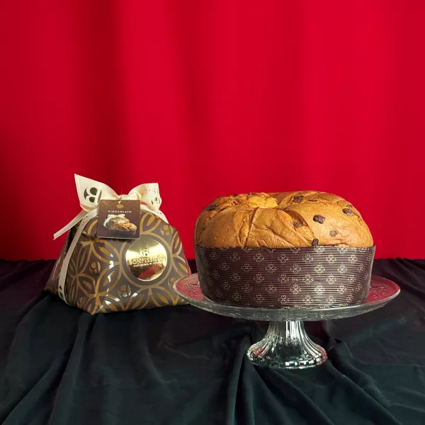 Panettone Chocolat Bonfissuto présenté sur un plat en cristal avec son coffret doré orné de motifs géométriques sur fond rouge festif