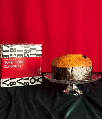Klassischer Panettone Olivieri auf einer Kristallplatte mit seiner typografischen rot-weißen Schachtel auf festlichem roten Hintergrund präsentiert