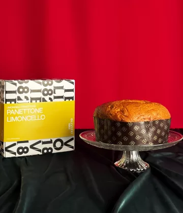 Panettone Limoncello Olivieri präsentiert auf einer Kristallplatte mit seiner typografischen gelb-weißen Schachtel auf festlich rotem Hintergrund