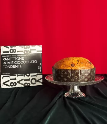 Panettone al cioccolato al rum Olivieri presentato su un piatto di cristallo con la sua scatola tipografica in bianco e nero su sfondo rosso festivo