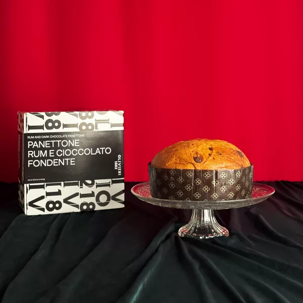 Panettone Rhum Chocolat Olivieri présenté sur un plat en cristal avec sa boîte noire et blanche typographique sur fond rouge festif