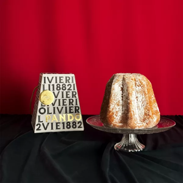 Pandoro Olivieri saupoudré de sucre glace présenté sur un plat en cristal avec sa boîte blanche typographique sur fond rouge festif