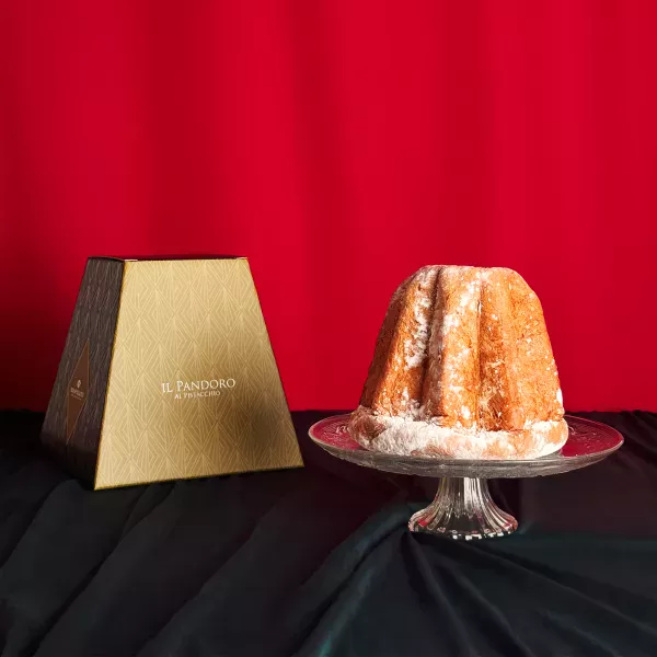 Pandoro Bonfissuto mit Puderzucker bestäubt präsentiert auf einer Kristallplatte mit seiner beige-braunen Pyramidenschachtel auf festlich rotem Hintergrund