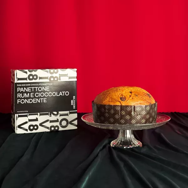 Panettone Rhum Chocolat Olivieri présenté sur un plat en cristal avec sa boîte noire et blanche typographique sur fond rouge festif